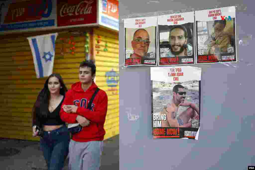 Una pareja camina junto a carteles con los rostros de los secuetrados por Hamás. Hoy ha comenzado un cele al fuego de cuatro días y serán liberados 50 rehenes que permanecen en Gaza.