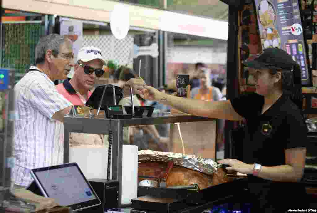 María Paula Solina ofrece una muestra de su producto a clientes ocasionales que se acercan al puesto de venta, en el Yellow Green Farmers Market, en Hollywood, Florida, el sábado 10 de junio de 2023. 