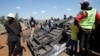 People stand next to a police vehicle that was burned during a demonstrations against the Kenya's proposed finance bill in Nairobi, Kenya, June 26, 2024. 