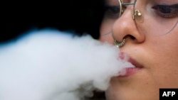 FILE - A woman blows smoke from an electronic cigarette in San Jose, Costa Rica, on May 14, 2024. 