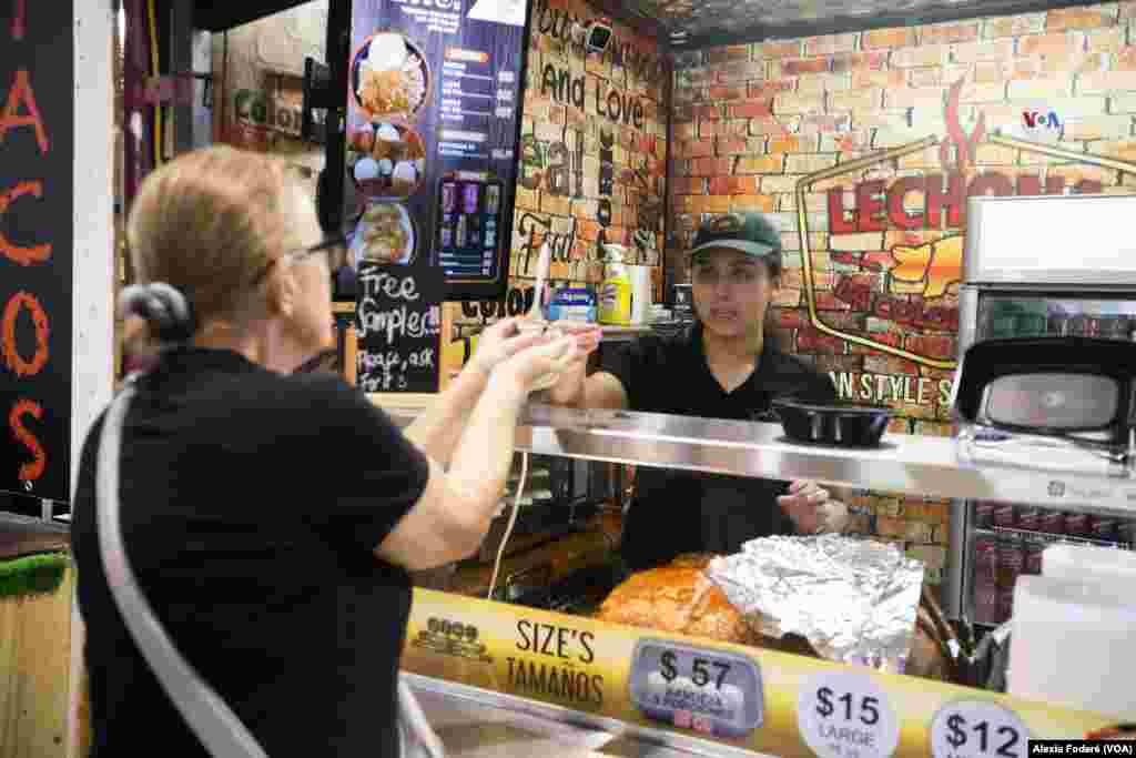 María Paula Solina, integrante del equipo de Lechona La Colombiana, departe con una cliente ocasional que se acerca al puesto de venta, en el Yellow Green Farmers Market, en Hollywood, Florida, el sábado 10 de junio de 2023. 