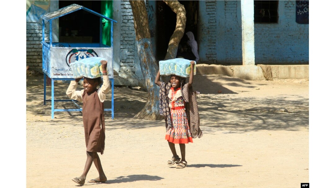 FILE - Children carry packs of humanitarian aid at a school housing displaced Sudanese who had fled violence in their war-torn country, near Gedaref, March 10, 2024.