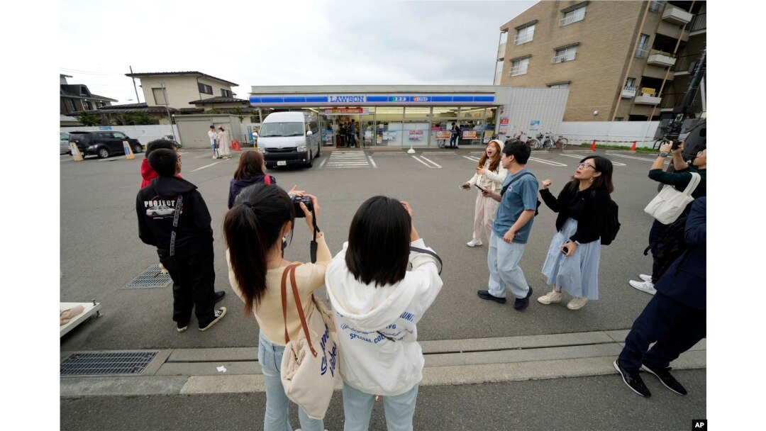 Tourists take pictures in front of the Lawson convenience store, a popular photo spot framing a picturesque view of Mt. Fuji in the background on cloudy evening of Tuesday, April 30, 2024, at Fujikawaguchiko town. (AP Photo/Eugene Hoshiko)
