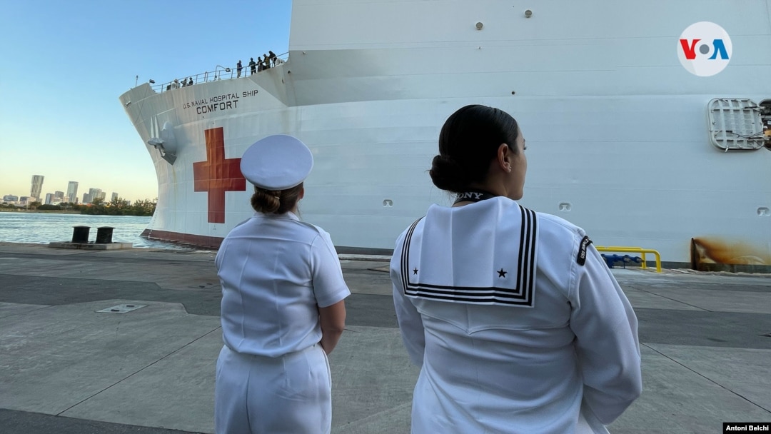 Dos miembros de la Marina de Estados Unidos esperan frente al buque hospital Comfort en el puerto de la ciuda de Miami, Florida, donde partirá hacia varios países de América Latina. Foto: Antoni Belchi / VOA.