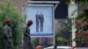 Pedestrians walk past a poster displaying Cameroonian President Paul Biya (R) next to his French counterpart Emmanuel Macron, in a street in Yaounde on July 25, 2022, prior to the French president's visit. 