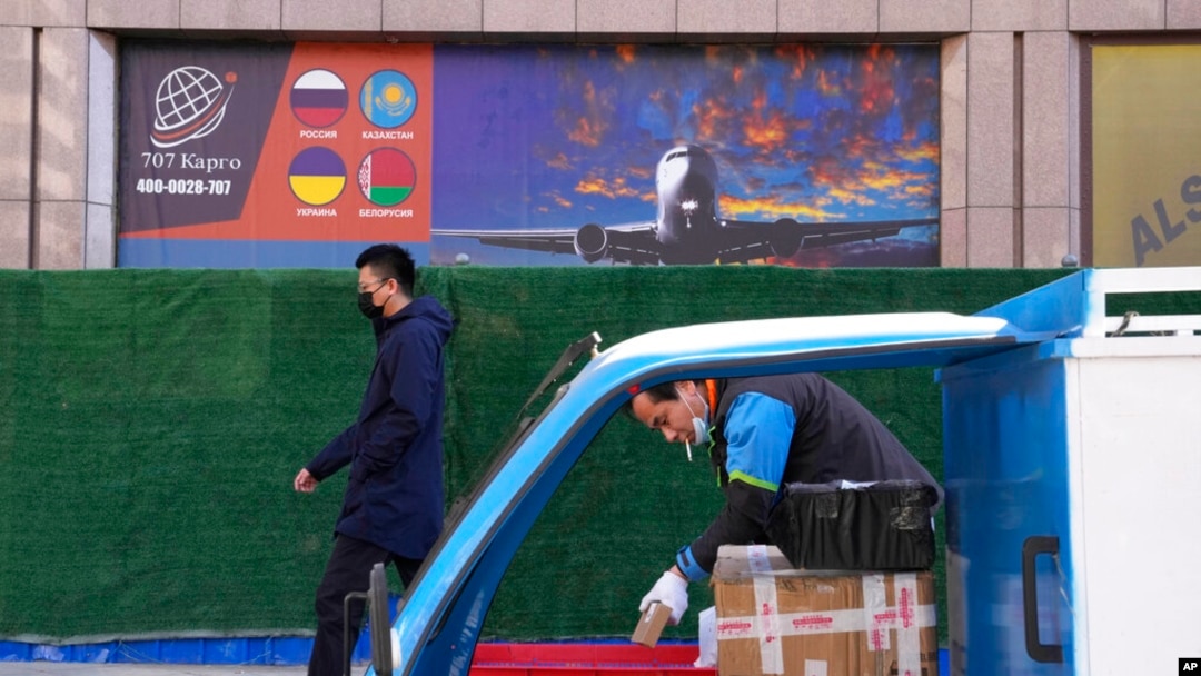 FILE - A deliveryman prepares packages as another man walks past an advertisement for cargo services at a trading center in Beijing, Feb. 26, 2022.