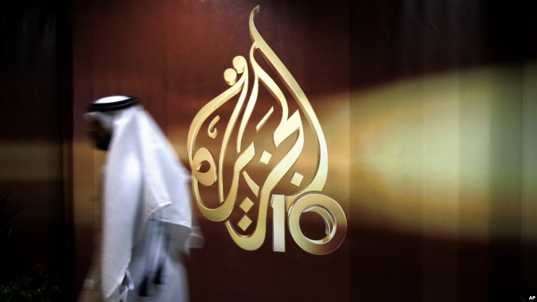 FILE - A Qatari employee of Al Jazeera Arabic language TV news channel walks past the network's logo, in Doha, Qatar, Nov. 1, 2006.
