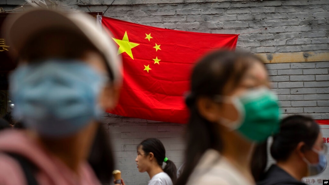 People walk past a Chinese flag on a tourist shopping street on the first day of the National Day holiday period in Beijing, Oct. 1, 2022. 