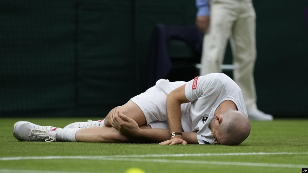 Adrian Mannarino of France lies on the ground in pain during the men's singles first round match against Switzerland's Roger Federer on day two of the Wimbledon Tennis Championships in London, Tuesday June 29, 2021. (AP Photo/Kirsty Wigglesworth)