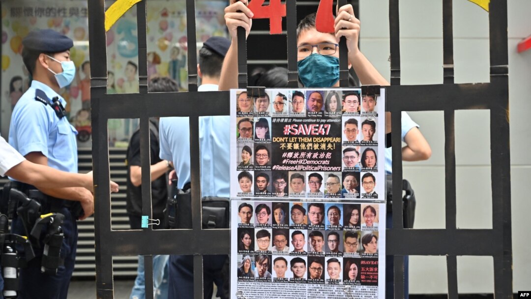 FILE - A protester stands behind mock jail bars with photos of imprisoned pro-democracy figures to be tried under the National Security Law, in Hong Kong, Sept. 19, 2021. 