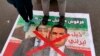 Anti-government protesters stand on a defaced poster with pictures of former Iraqi Prime Minister Nouri al-Maliki, left, and Iraq's Prime Minister-designate Adnan Al-Zurfi, in Tahrir Square, March 18, 2020.