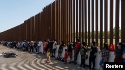 FILE - Asylum-seeking migrants, mostly from Venezuela and Cuba, wait to be transported by U.S. Customs and Border Protection agents after crossing the Rio Grande River into the U.S. from Mexico at Eagle Pass, Texas, July 14, 2022. 