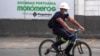 ARCHIVO - Un trabajador pedalea en su bicileta cerca de una valla con el logo de la firma Monómeros, en Barranquilla, Colombia, el 9 de octubre de 2021.