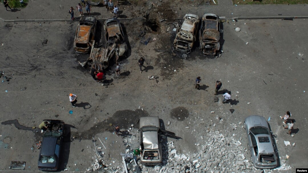 People stand next to cars destroyed by a Russian missile strike at a residential area in Kharkiv, Ukraine, June 26, 2022. 