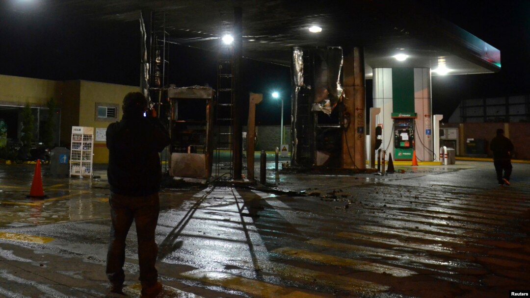 A plainclothes Mexican police officer takes pictures with his cellphone of a gas station following an arson attack in Morelia, Oct. 27, 2013. 