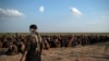 FILE - U.S.-backed Syrian Democratic Forces (SDF) fighters stand guard next to men waiting to be screened after being evacuated out of the last territory held by Islamic State group militants, near Baghouz, eastern Syria. 