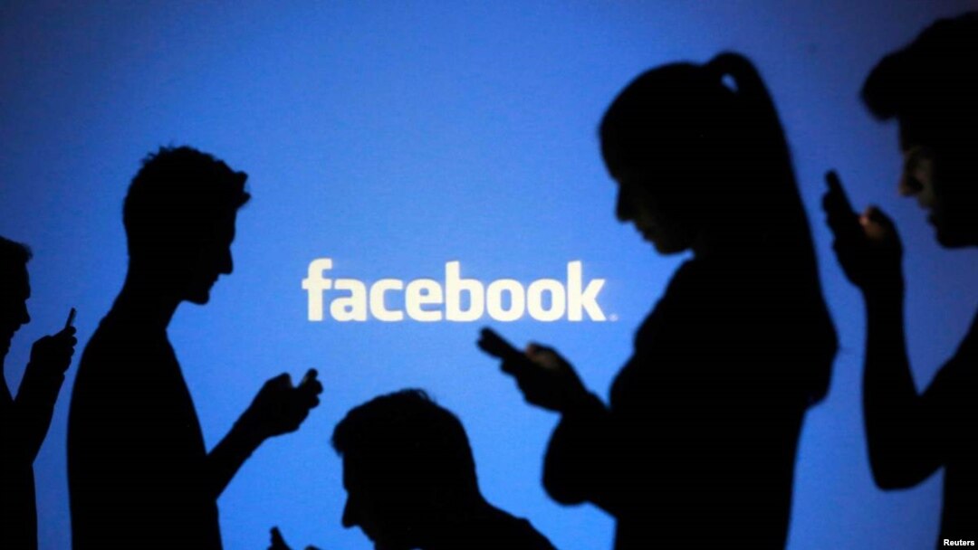 FILE - People are silhouetted as they pose with laptops in front of a screen projected with a Facebook logo, file photo. 