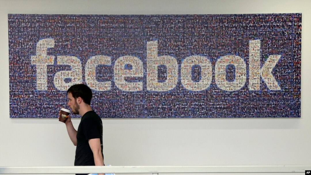 FILE - A Facebook employee walks past a sign at Facebook headquarters in Menlo Park, California. 
