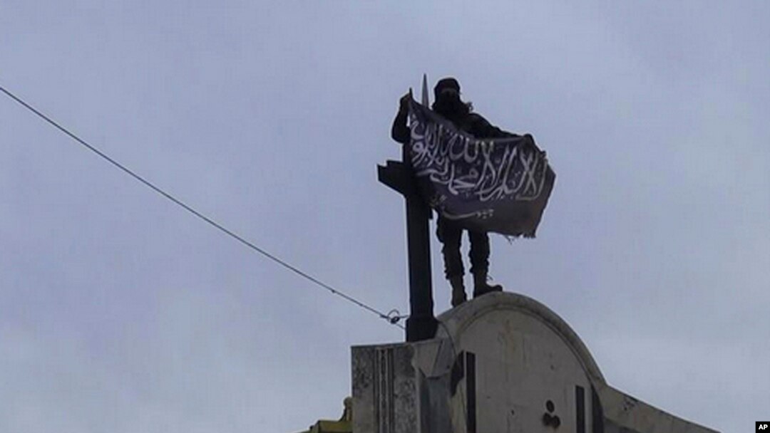 In this image posted on the Twitter page of Syria's al-Qaida-linked Nusra Front on Saturday, March 28, 2015, which is consistent with AP reporting, a fighter from Syria's al-Qaida-linked Nusra Front holds his group flag in Idlib province, north Syria.