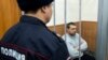 FILE - Former Russian police officer Denis Konovalov, right, sits in a cage prior to a court hearing in Moscow, Russia, Jan. 30, 2020.