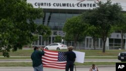 FILE - Men hold a sign and a U.S. flag across the street from the Curtis Culwell Center, where two men opened fire at an event soliciting cartoons of the Prophet Mohammad, in Garland, Texas, May 5, 2015.