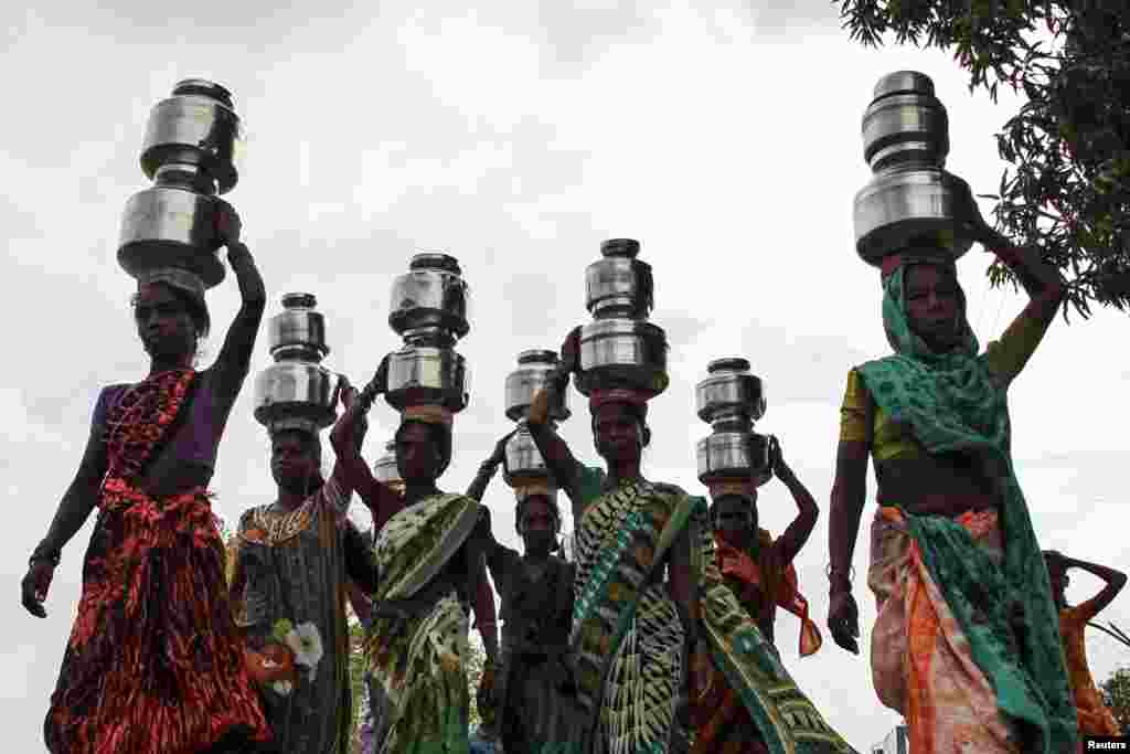 Women carry pitchers filled with water from an opening made to filter water in Thane, India.