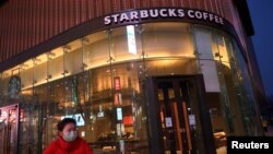 A woman wearing a face mask rides a bicycle past a Starbucks coffee store, as the country is hit by an outbreak of the novel coronavirus, in Beijing, China, Feb. 20, 2020.