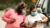 FILE -- Women wear masks as they check a mobile phone in Houston, Texas.