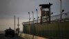 FILE - A U.S. soldier stands in the turret of a vehicle with a machine gun, left, as a guard looks out from a tower at the Guantanamo Bay prison in Cuba, March 30, 2010.