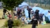 French police officers watch migrants packing their belongings in a camp of Grande Synthe, northern France, Tuesday, Sept.17, 2019.