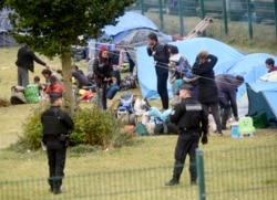FILE - French police officers watch migrants packing their belongings in a camp of Grande Synthe, northern France, Sept.17, 2019.