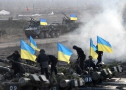 FILE - Ukrainian servicemen are seen standing on top of tanks during a drill in Ukraine's Zhytomyr region, Nov. 21, 2018.