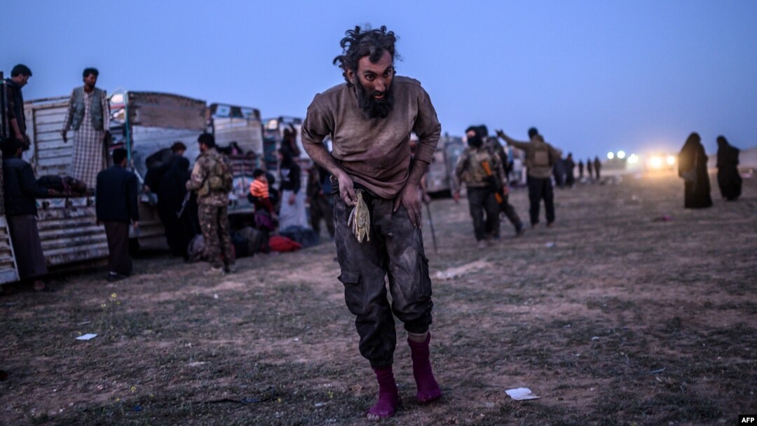 A man suspected of belonging to the Islamic State group walks past members of the Kurdish-led Syrian Democratic Forces just after leaving IS' last holdout of Baghuz, in the eastern Syrian province of Deir Ezzor, March 4, 2019. 