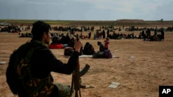 FILE - A member of U.S.-backed Syrian Democratic Forces (SDF) watches over people who were evacuated out of the last territory held by Islamic State militants, outside Baghouz, Syria, March 5, 2019.
