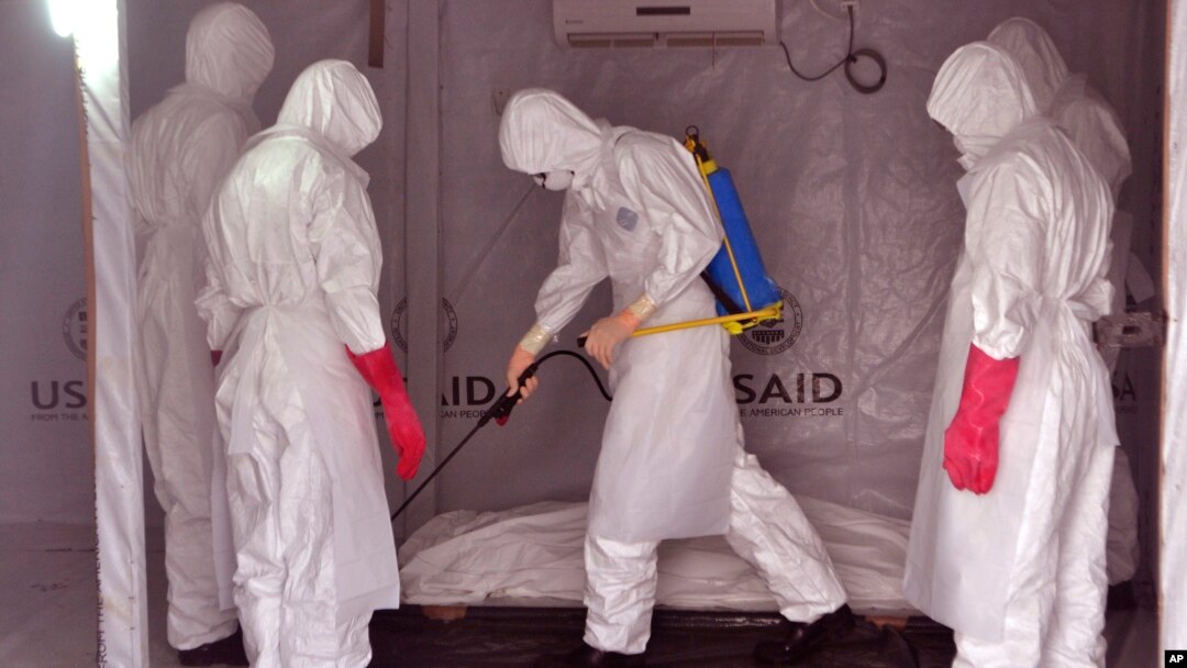 Health workers wearing protective gear spray the shrouded body of a man with disinfectant as they suspect he died from the Ebola virus, at a USAID, American aid Ebola treatment center at Tubmanburg on the outskirts of Monrovia, Liberia, Nov. 28, 2014.