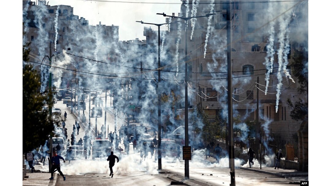 Palestinian stone throwers run to take cover after Israeli security forces fired tear gas canisters during clashes following a demonstration next to the Israeli controversial separation wall in the West Bank city of Bethlehem, Dec. 18, 2015.