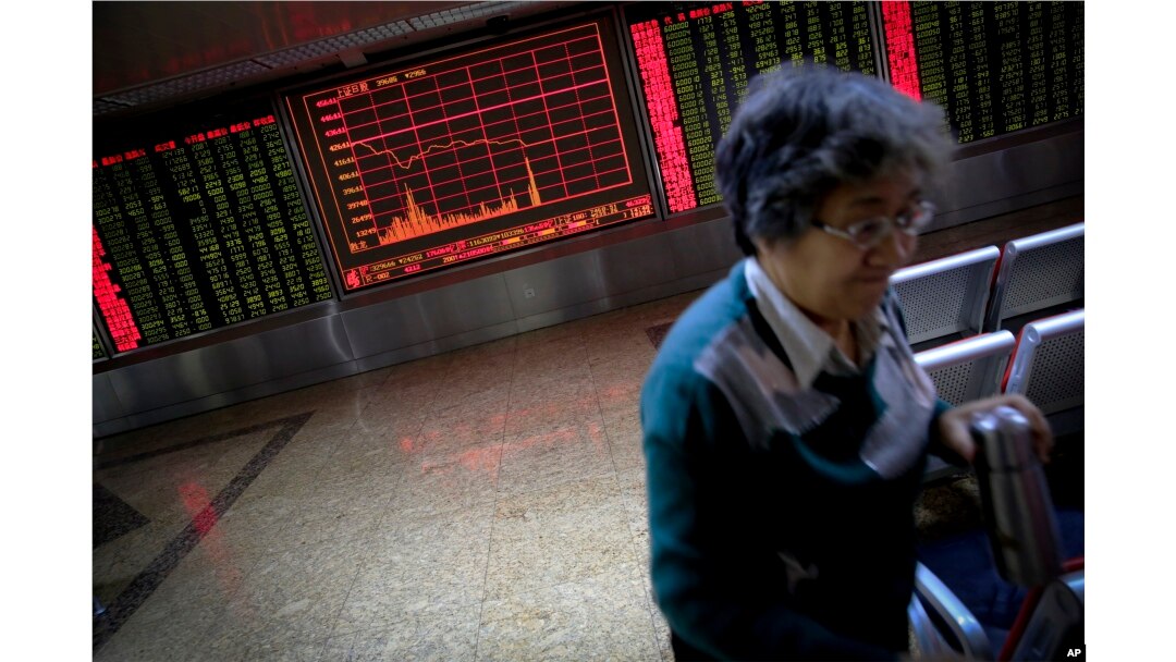 A woman walks past an electronic board displaying stock prices as she leaves a brokerage house in Beijing, Monday, Jan. 4, 2016.