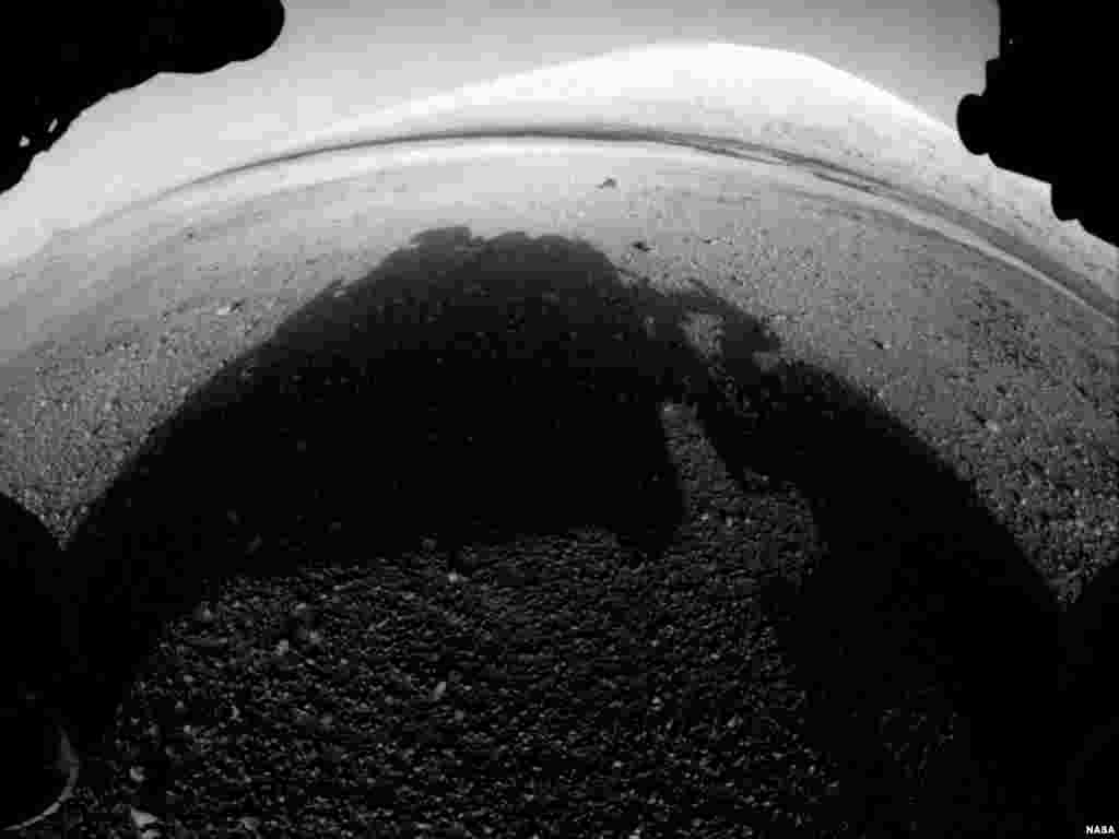 This image shows what lies ahead for the rover -- its main science target, informally called Mount Sharp. The rover's shadow is seen in the foreground, and the dark bands beyond are dunes. In the distance is the highest peak of Mount Sharp.