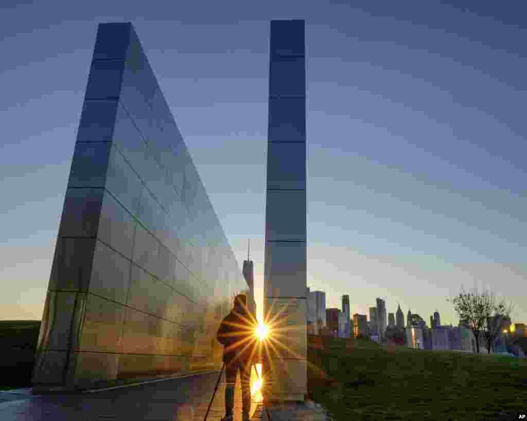 The light reflects off of the Empty Sky Memorial in Jersey City, New Jersey, as the sun rises over the New York City skyline, across the Hudson River.