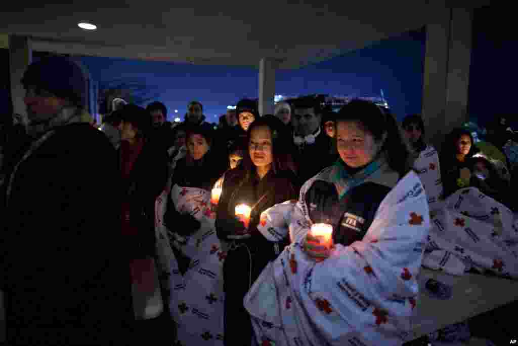 2012年12月16日,在奧巴馬總統在紐敦高中舉行的一次跨教派燭光守夜儀式上講話之際,居民們在校外舉著蠟燭紀念桑迪.胡克小學槍擊案遇難者。