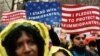 FILE - People hold signs before marching to Trump Tower in a protest organized by the New York Immigration Coalition against President-elect Donald Trump in New York, Dec. 18, 2016.