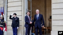 New French prime minister Michel Barnier, right, shakes hands with outgoing prime minister Gabriel Attal during the handover ceremony, Sept. 5, 2024 in Paris. 