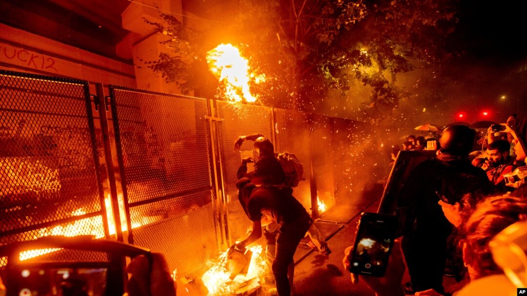 Protesters throw flaming debris over a fence at the Mark O. Hatfield United States Courthouse on Wednesday, July 22, 2020, in Portland, Ore. Following a larger Black Lives Matter Rally, several hundred demonstrators faced off against federal…