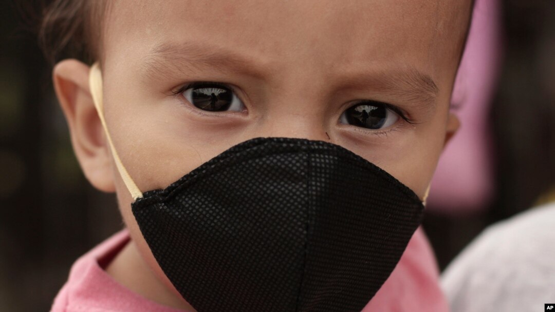 Gael Gómez, de un año de edad, usa una máscara para evitar la propagación del coronavirus, mientras su madre lo abraza y pide comida a los conductores en la Carretera Dorada en Ilopango, El Salvador.