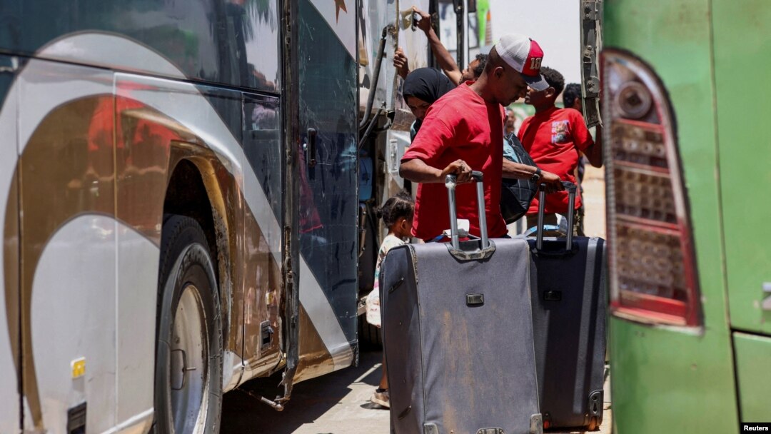 People stand next to buses as passengers fleeing from Sudan arrive at the Argeen land port, after being evacuated from Khartoum to Abu Simbel city, at the upper reaches of the Nile in Aswan