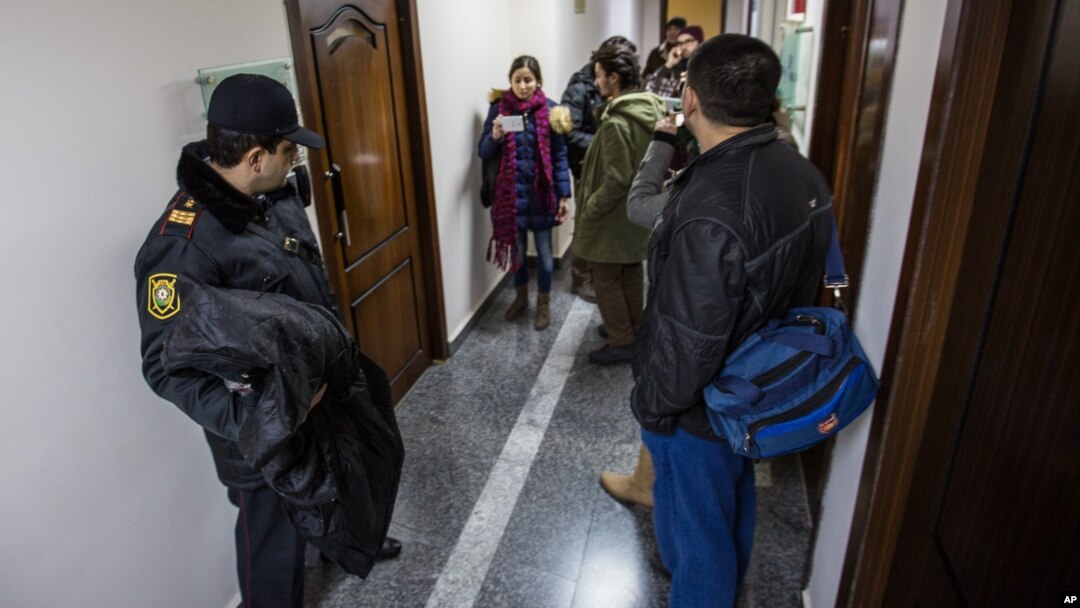 FILE - An Azerbaijani policeman, left, guards as journalists gather at the Radio Free Europe headquarters in Baku, Dec. 26, 2014.