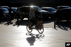 FILE - Commuters ride bicycles past cars clogged with heavy traffic during the morning rush hour in the Central Business District of Beijing, China, Nov. 15, 2017.