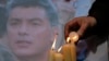 People light candles in memory of Boris Nemtsov, seen behind, at the monument of political prisoners 'Solovetsky Stone' in central St. Petersburg, Russia, Feb. 28, 2015
