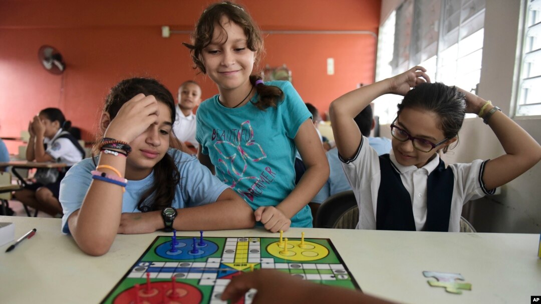 In this Friday, Oct. 13, 2017 photo, girls play a board game at the Ramon Marin Sola Elementary School, which opened its doors as a daytime community center after the passing of Hurricane Maria in Guaynabo, Puerto Rico. (AP Photo/Carlos Giusti)