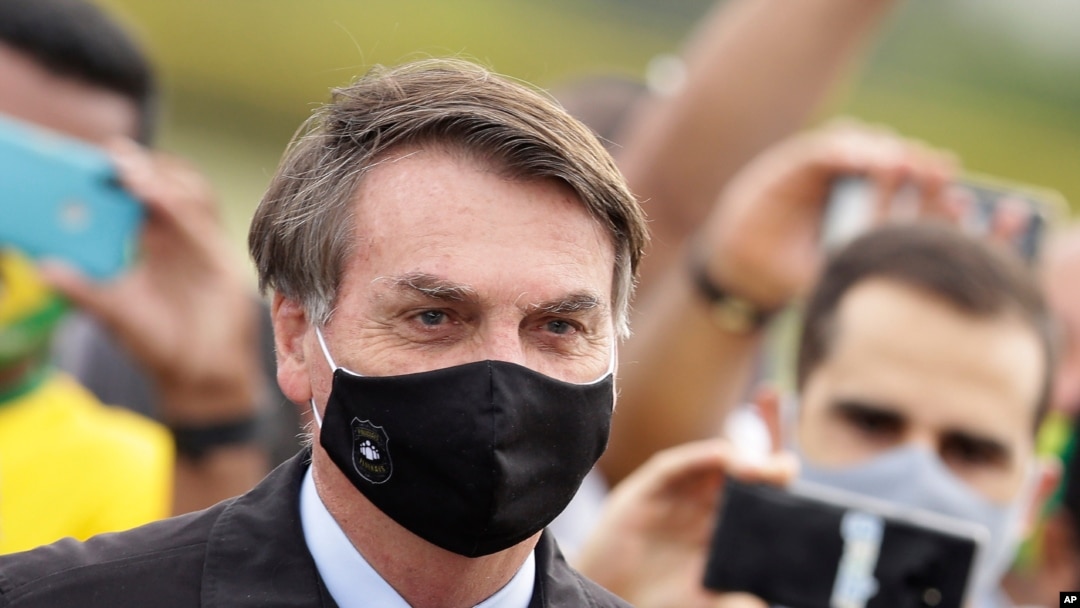 El presidente de Brasil, Jair Bolsonaro, se encuentra en medio de partidarios que toman fotos con teléfonos celulares cuando sale de su residencia oficial.